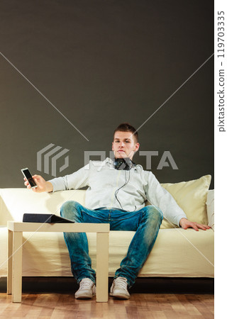 man on couch with headphones smartphone and tablet 119703335