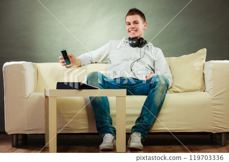 man on couch with headphones smartphone and tablet 119703336