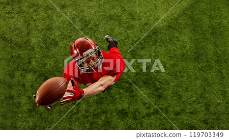 Top view image of concentrated man, American football player in red uniform in motion on stadium, catching ball with precision Top view image of concentrated man, American football player in red uniform in motion on stadium, catching ball with precision 119703349