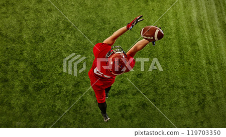 Top view image of concentrated man, American football player in red uniform in motion on stadium, catching ball with precision Top view image of concentrated man, American football player in red uniform in motion on stadium, catching ball with precision 119703350