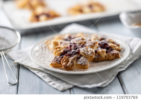 Sweet dessert pastries made of puff pastry with strawberry jam filled with caramelized apple sprinkled with powdered sugar Sweet dessert pastries made of puff pastry with strawberry jam filled with caramelized apple sprinkled with powdered sugar 119703769