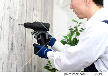 A young Asian man in an apron using an electric screwdriver/electric drill A young Asian man in an apron using an electric screwdriver/electric drill 119704913