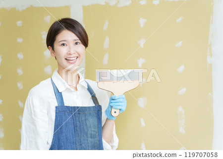 A DIY girl applying putty to plasterboard 119707058