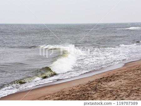 Waves are crashing on a beautiful sandy beach on a cloudy day 119707389