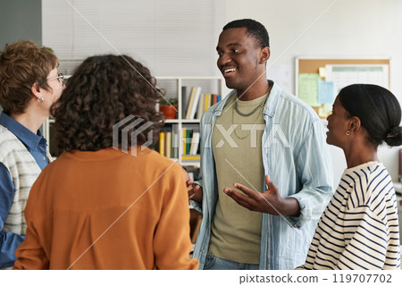 Group of multiracial colleagues laughing during light-hearted conversation in modern office setting with bookshelves and documents in background Group of multiracial colleagues laughing during light-hearted conversation in modern office setting with bookshelves and documents in background 119707702