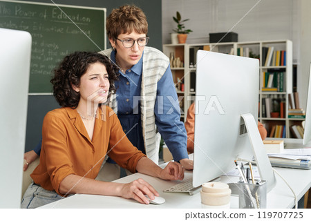 Two people collaborating on educational project in modern office, using desktop computer. Man and woman discussing details and looking at screen intensely 119707725