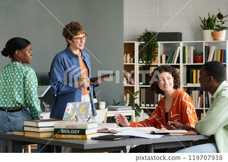 Group of diverse students engaging in collaborative discussion while working on a group project in a modern classroom filled with books and plants 119707938
