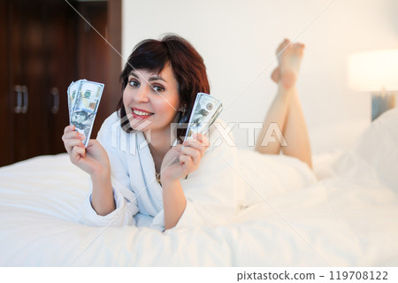 Rich beautiful woman counting cash while lying in bed in hotel 119708122