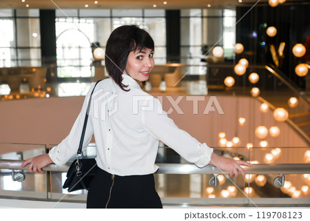 Girl with bob haircut in white blouse near big staircase with chandelier 119708123
