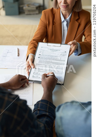 Vertical closeup of unrecognizable Black man signing tax declaration form during consultation with personal finance advisor Vertical closeup of unrecognizable Black man signing tax declaration form during consultation with personal finance advisor 119708204