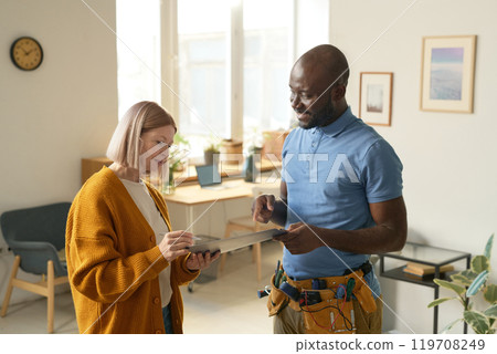 Side view portrait of smiling African American man handing clipboard to female client signing contract for home repairs services copy space Side view portrait of smiling African American man handing clipboard to female client signing contract for home repairs services copy space 119708249