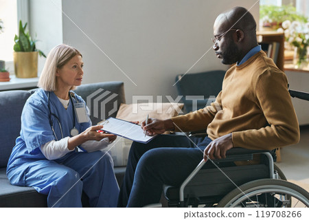 Side view portrait of African American man with disability signing medical form during at home doctors visit copy space Side view portrait of African American man with disability signing medical form during at home doctors visit copy space 119708266