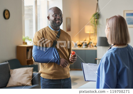 Waist up portrait of smiling adult African American man with broken arm talking to nurse after successful at home med visit copy space Waist up portrait of smiling adult African American man with broken arm talking to nurse after successful at home med visit copy space 119708271
