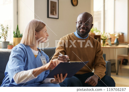 Portrait of adult African American man signing contract on clipboard for at home medical services and smiling during doctors visit 119708287