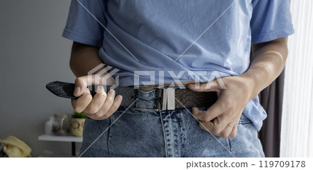 Hands unbuttoning leather belt on jeans 119709178