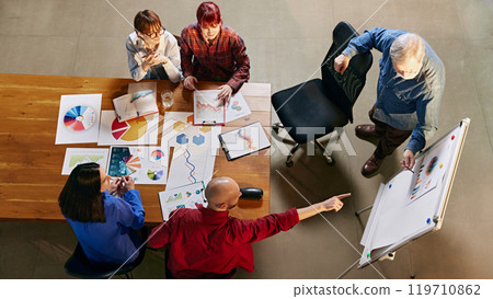 Office meeting with data-driven discussion. Aerial view of corporate professionals review financial graphs and future projections. Office meeting with data-driven discussion. Aerial view of corporate professionals review financial graphs and future projections. 119710862