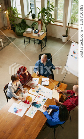 Team meeting focused on analyzing market data, as professionals discuss new ideas and corporate strategies. Top-down view. Team meeting focused on analyzing market data, as professionals discuss new ideas and corporate strategies. Top-down view. 119710865