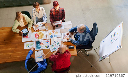 Aerial view of diverse team of professionals collaborating on market insights, using charts and data to plan for growth. Aerial view of diverse team of professionals collaborating on market insights, using charts and data to plan for growth. 119710867