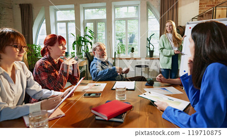 Group of business professionals carefully reviewing reports and data around conference table in modern office. Corporate discussions. Group of business professionals carefully reviewing reports and data around conference table in modern office. Corporate discussions. 119710875