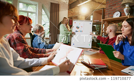 Group portrait. Project leader outlines strategic plan on whiteboard, with team members actively engaged in discussion in modern meeting room. Group portrait. Project leader outlines strategic plan on whiteboard, with team members actively engaged in discussion in modern meeting room. 119710877