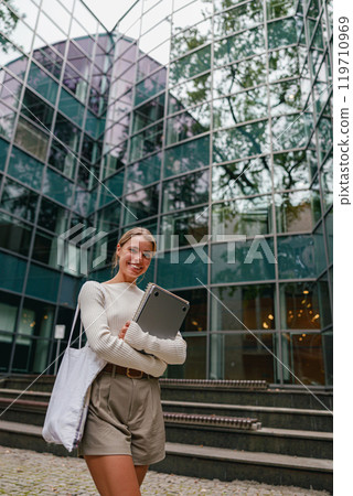 A young woman is seated in a modern urban setting, working diligently on her laptop A young woman is seated in a modern urban setting, working diligently on her laptop 119710969