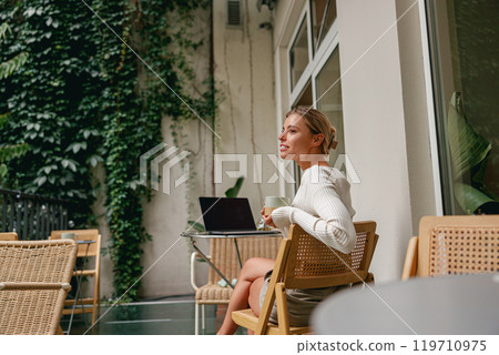 Woman Working Outdoors on Laptop in Cozy Caf Setting 119710975