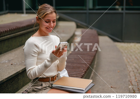 A young woman is actively engaged with her smartphone while enjoying an urban setting atmosphere A young woman is actively engaged with her smartphone while enjoying an urban setting atmosphere 119710980