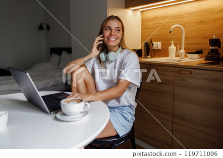 A Young Woman Engaged in Remote Work, Utilizing Her Laptop and Enjoying Coffee in a Cozy Space 119711006