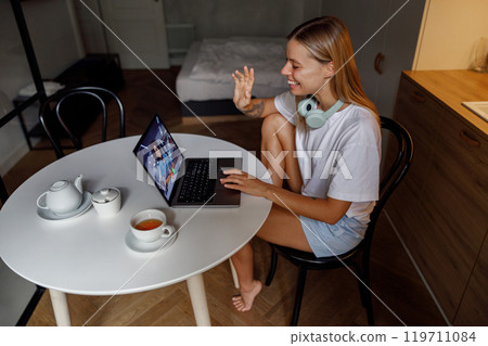 A young woman is engaged in video calling while situated comfortably in a modern workspace 119711084