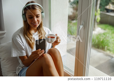 A Relaxed Young Woman Enjoying a Cup of Tea While Listening to Soothing Music at Home A Relaxed Young Woman Enjoying a Cup of Tea While Listening to Soothing Music at Home 119711110