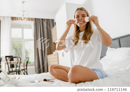 A Smiling Woman Happily Enjoying Her Morning Skincare Routine in a Bright and Cozy Bedroom A Smiling Woman Happily Enjoying Her Morning Skincare Routine in a Bright and Cozy Bedroom 119711146
