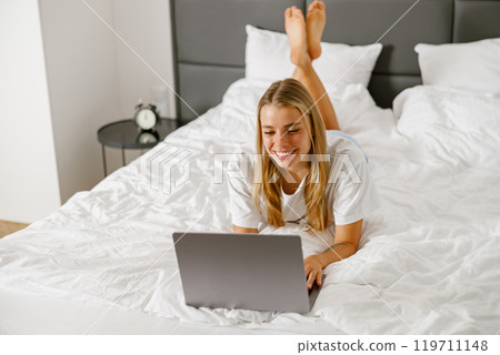 A Relaxing Young Woman Who Is Working on Her Laptop While Comfortably Sitting in Bed 119711148