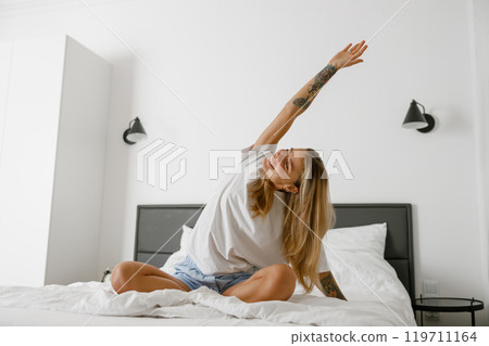 Engaging in a Morning Stretch in a Cozy Bedroom Setting for Overall Wellness and Relaxation Benefits 119711164