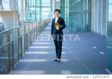 A middle-aged business woman in a suit standing in a hallway A middle-aged business woman in a suit standing in a hallway 119711475