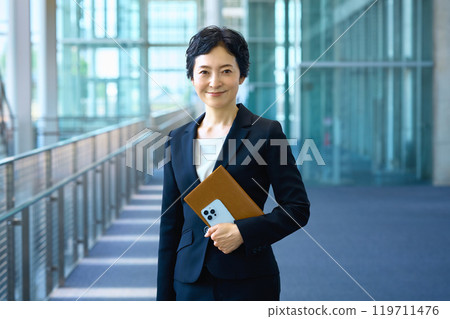 A middle-aged business woman in a suit standing in a hallway 119711476