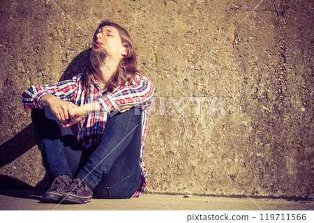 Man long haired sitting alone sad on grunge wall Man long haired sitting alone sad on grunge wall 119711566