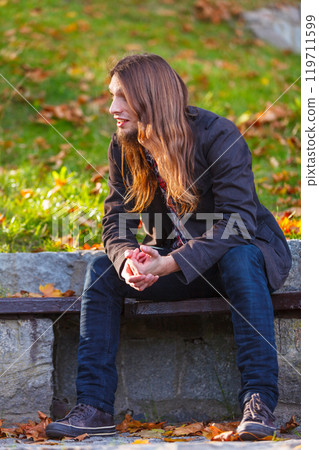 Man long hair sitting on bench in autumn park 119711599