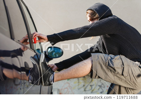 Thieft man holding screwdriver breaking into car Thieft man holding screwdriver breaking into car 119711688