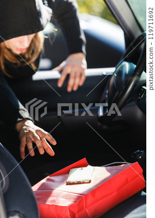 Burglar thief stealing smartphone and bag from car Burglar thief stealing smartphone and bag from car 119711692