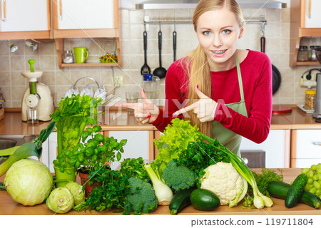 Woman in kitchen having many green vegetables 119711804