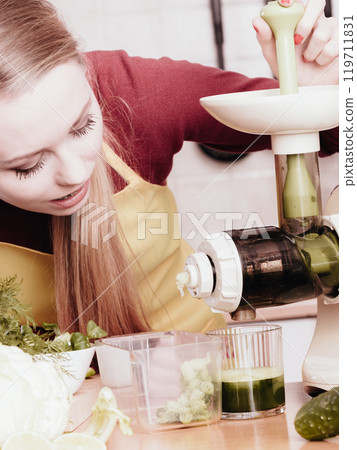 Woman in kitchen making vegetable smoothie juice 119711831