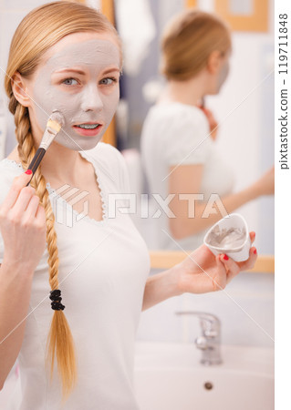 Happy young woman applying mud mask on face Happy young woman applying mud mask on face 119711848