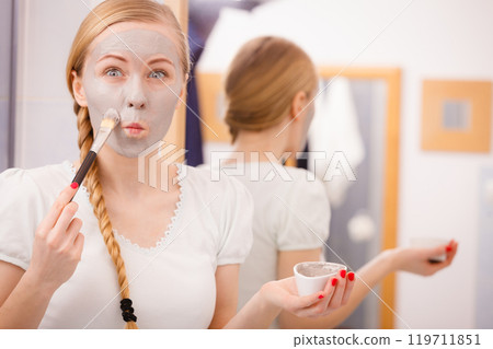 Happy young woman applying mud mask on face Happy young woman applying mud mask on face 119711851