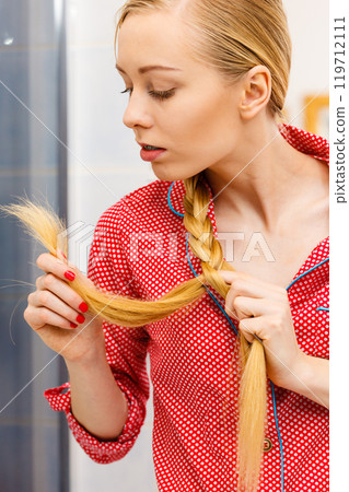 Blonde woman looking at her hair ends Blonde woman looking at her hair ends 119712111