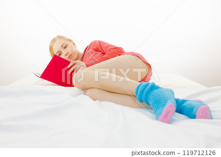 Woman relaxing in bed reading book Woman relaxing in bed reading book 119712126
