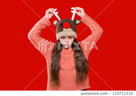Teenage girl in Xmas hat isolated on red. Winter fashion for teenage style. Girl in knitted hat in winter season. Childhood lifestyle. Winter child wardrobe. Knitted accessories Teenage girl in Xmas hat isolated on red. Winter fashion for teenage style. Girl in knitted hat in winter season. Childhood lifestyle. Winter child wardrobe. Knitted accessories 119712318