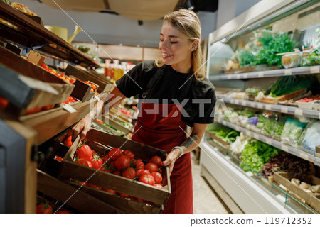 A Young Female Employee is Organizing and Arranging Bright Fresh Produce in a Grocery Store A Young Female Employee is Organizing and Arranging Bright Fresh Produce in a Grocery Store 119712352