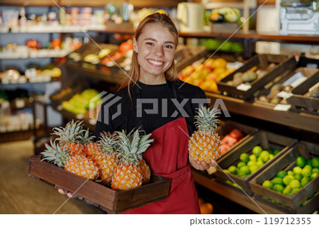 A Cheerful Worker Holding Fresh Pineapples While Working in a Grocery Store Environment 119712355