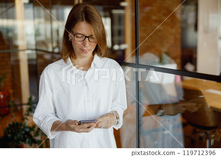 A woman is utilizing her smartphone in a modern office environment that promotes productivity A woman is utilizing her smartphone in a modern office environment that promotes productivity 119712396