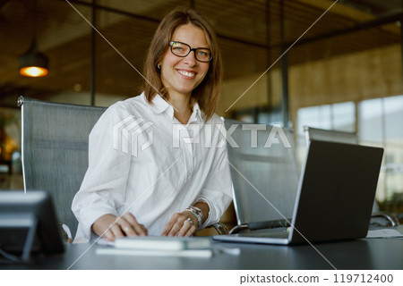 A Professional Businesswoman Wearing Glasses in a Contemporary Office Setting with a Laptop 119712400